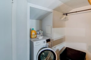 Een kleine wasruimte met een voorlader wasmachine, een droogrek en een plank met schoonmaakmiddelen.