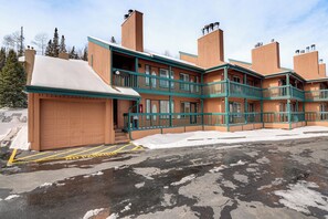 Un immeuble à plusieurs étages doté d’un garage, de balcons et d’un sol recouvert de neige.