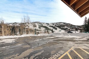 Un parking dont le sol est recouvert de neige, offrant une vue sur une région montagneuse avec des arbres et des bâtiments en arrière-plan.