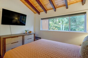 A bedroom with a bed, a TV mounted on the wall, a window with a view of trees, and a wooden ceiling. - Cozy Brianhead Condo: Easy Walk to Giant Steps (Brian Head)