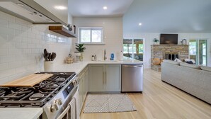 Een moderne keuken met een gasfornuis, vaatwasser en een inbouwoven. Er is een groot raam dat natuurlijk licht en uitzicht op de omgeving biedt.