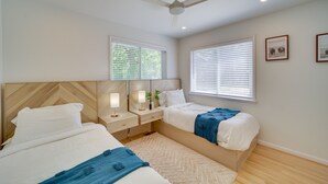 Een slaapkamer met twee bedden, een plafondventilator en twee ramen met zonwering.