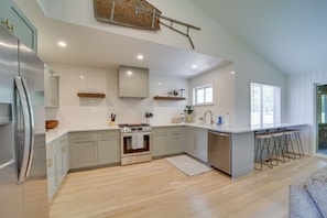 Una cocina moderna con un refrigerador de acero inoxidable, horno integrado y un lavamanos. Hay taburetes de madera en la isla y una ventana que proporciona luz natural.