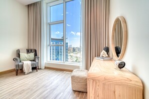 Une chambre d’hôtel moderne dotée d’une grande fenêtre, d’un fauteuil confortable, d’une coiffeuse en bois et d’un miroir rond.