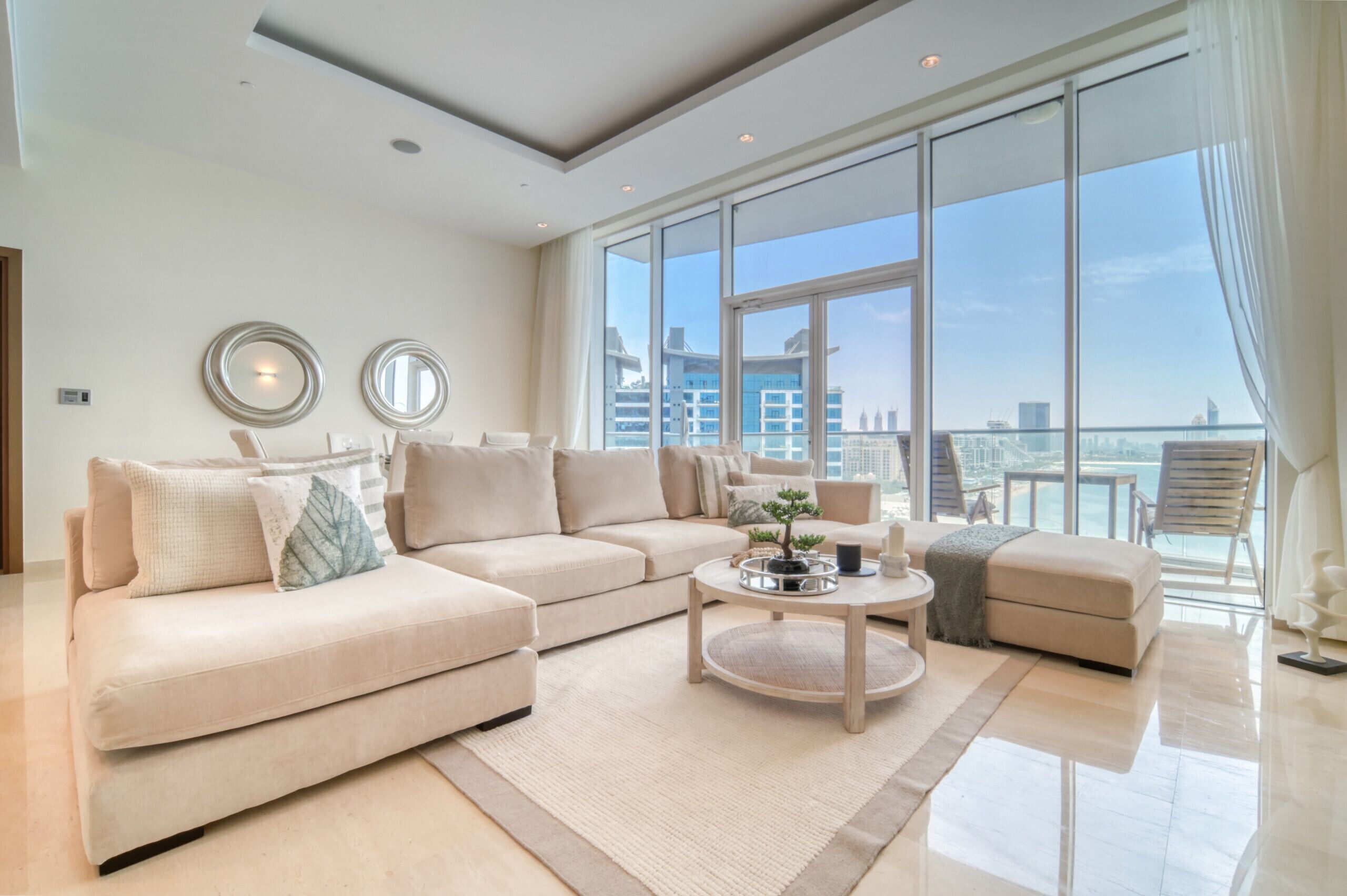 A modern living room with a sectional sofa, a round coffee table, and a view of the city through large windows.