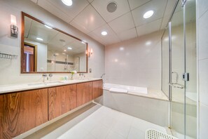 A modern bathroom with a wooden vanity, a large mirror, a glass shower enclosure, and a white bathtub.