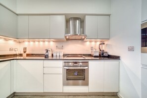 A modern kitchen with white cabinetry, stainless steel appliances, and under-cabinet lighting.