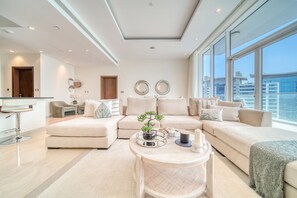 Un salon moderne avec un canapé d’angle, une table basse ronde et une vue sur les gratte-ciel de la ville, visible à travers de grandes fenêtres.