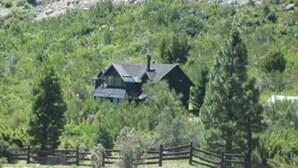 A house surrounded by dense greenery, with a wooden fence in the foreground.