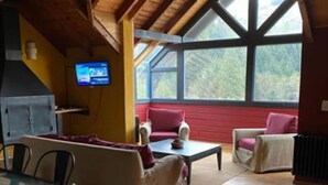 A cozy room with a wooden ceiling, a television mounted on the wall, and a large window offering a view of the outdoors.