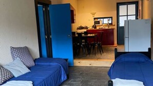 Et lille, kompakt værelse med to senge, et tekøkken og en dør til et badeværelse.