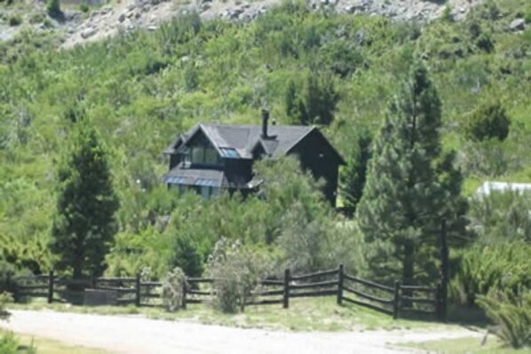 Ein Haus, umgeben von dichtem Grün, mit einem Holzzaun im Vordergrund.
