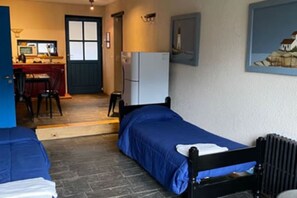 Ein Schlafzimmer mit zwei Einzelbetten, einer kleinen Küchenzeile und einer Tür zum Badezimmer.