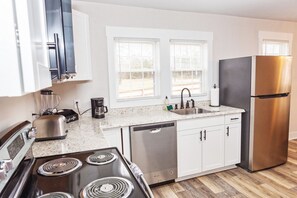 A modern kitchen with white cabinets, a stainless steel refrigerator, a dishwasher, a stove, and a coffee maker.