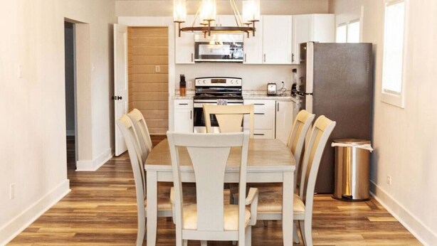 A modern kitchen with white cabinets, a stainless steel refrigerator, and a dining area with a wooden table and chairs. - Salem Road Ranch | 3 BR w/ Outdor Firepit and Backyard (Lincolnton)