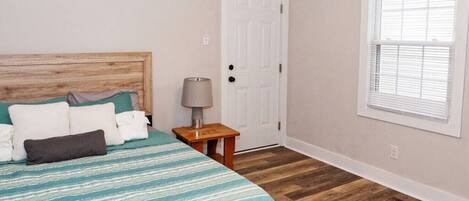 A bedroom with a bed, a nightstand, a door, and a window.