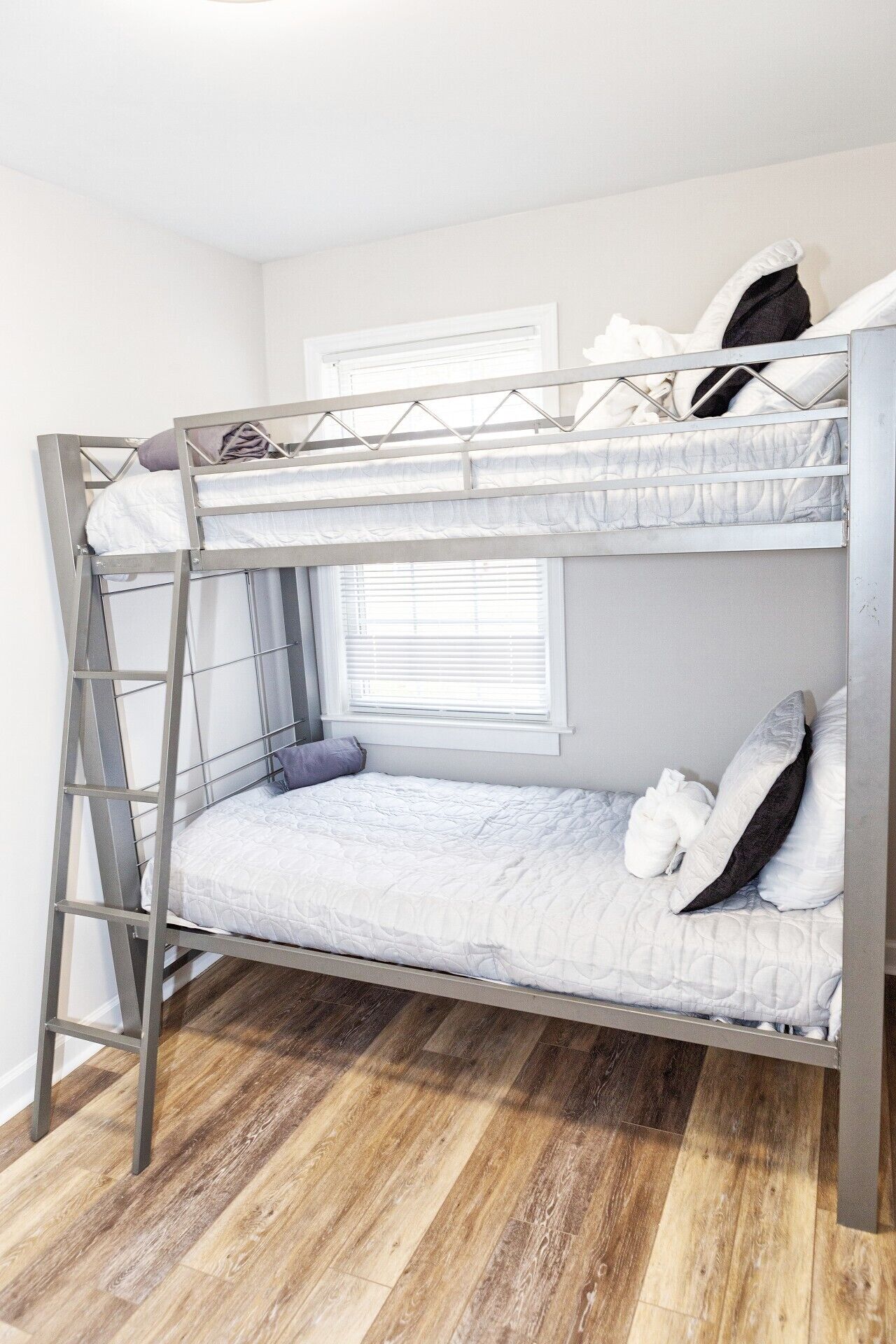 A bunk bed with a ladder, a window with blinds, and a wooden floor.