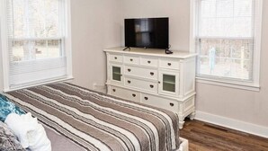 A bedroom with a bed, a dresser, a television, and two windows. - Salem Road Ranch | 3 BR w/ Outdor Firepit and Backyard (Lincolnton)