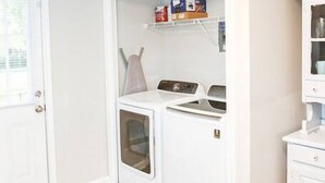 Une buanderie équipée d’un lave-linge, d’un sèche-linge et d’étagères contenant des produits de lessive.