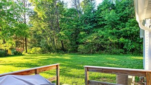 Une terrasse avec un lit et une table, donnant sur une cour verdoyante bordée d’arbres.