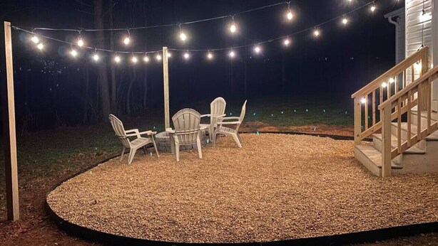 An outdoor patio with string lights, a wooden deck, and a small table with chairs. - Outdoorsy Escape~3BR/2BA House~Huntersville with Firepit and Huge Backyard! (Huntersville)