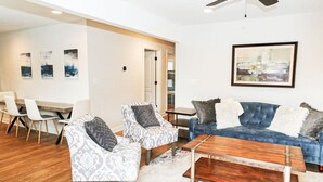A living room with a blue sofa, patterned armchairs, a wooden coffee table, and a dining area with a white table and chairs. - Outdoorsy Escape~3BR/2BA House~Huntersville with Firepit and Huge Backyard! (Huntersville)