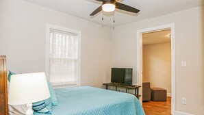 A bedroom with a bed, a TV on a stand, a ceiling fan, and a door leading to another room. - Outdoorsy Escape~3BR/2BA House~Huntersville with Firepit and Huge Backyard! (Huntersville)