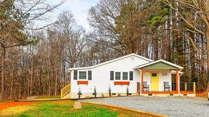 A single-story white building with a porch, numbered 7519, surrounded by trees. - Outdoorsy Escape~3BR/2BA House~Huntersville with Firepit and Huge Backyard! (Huntersville)