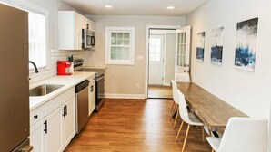 A modern kitchen with white cabinets, a red coffee maker, and a wooden dining table with chairs. - Outdoorsy Escape~3BR/2BA House~Huntersville with Firepit and Huge Backyard! (Huntersville)