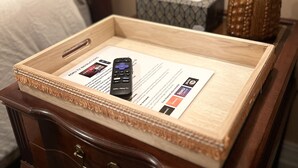A wooden tray with a remote control and a Roku TV instruction manual on a bedside table.