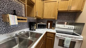 A kitchen with wooden cabinets, a stainless steel sink, a microwave, a coffee maker, and a stove.