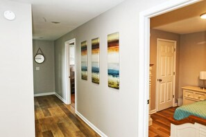 Un pasillo con piso de madera, una puerta que da a un dormitorio y una pared con tres cuadros de paisajes.