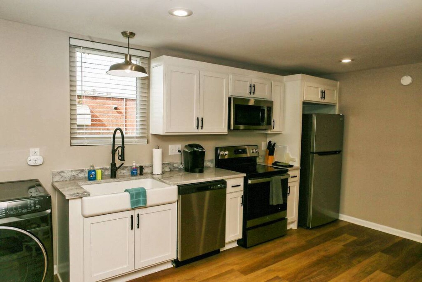 Una cocina compacta con gabinetes blancos, un refrigerador de acero inoxidable, un microondas, un lavavajillas y una estufa.