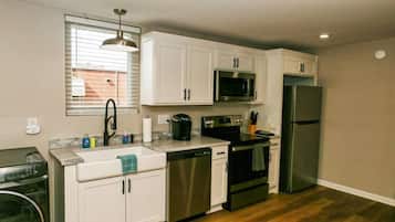 Una cocina compacta con gabinetes blancos, un refrigerador de acero inoxidable, un microondas, un lavavajillas y una estufa.