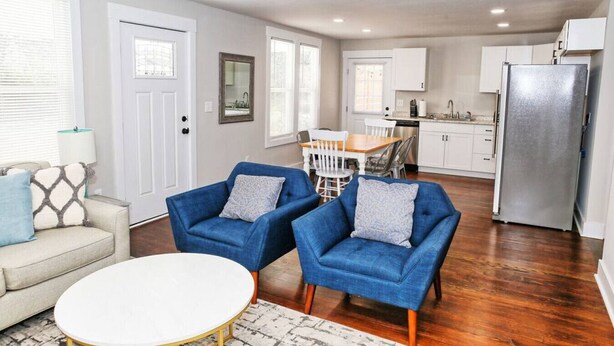 A modern living room with a sofa, two armchairs, a coffee table, and a dining area with a table and chairs.