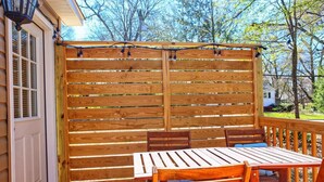 A wooden deck with a table and chairs, surrounded by a wooden fence with string lights.
