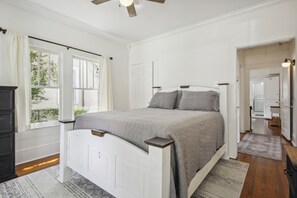 Une chambre à coucher comprenant un lit, une commode, une fenêtre avec des rideaux et une porte donnant sur une salle de bain.