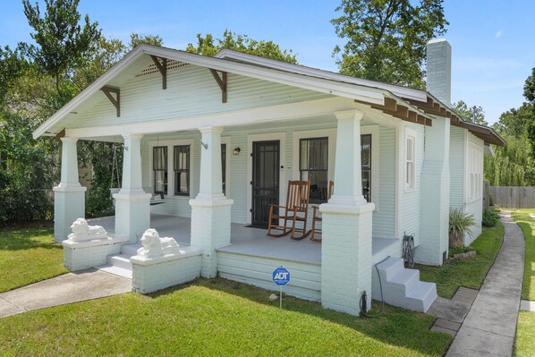 Een wit huis met één verdieping, een veranda, schoorsteen en een kleine tuin.