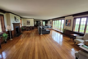 A spacious living room with hardwood floors, a fireplace, a sofa, and large windows offering a view of the outdoors. - 8 bedroom seacoast manor with amazing views! (South Kingstown)