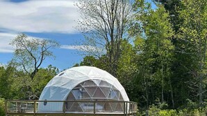 A dome-shaped structure with a wooden deck, surrounded by a grassy field and trees. - Dome 1 - Luxury Dome at Come Spring Farm (Union)