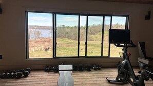 A spacious room with a large window overlooking a grassy field and a body of water. There are exercise equipment including a stationary bike and dumbbells. - Dome 1 - Luxury Dome at Come Spring Farm (Union)