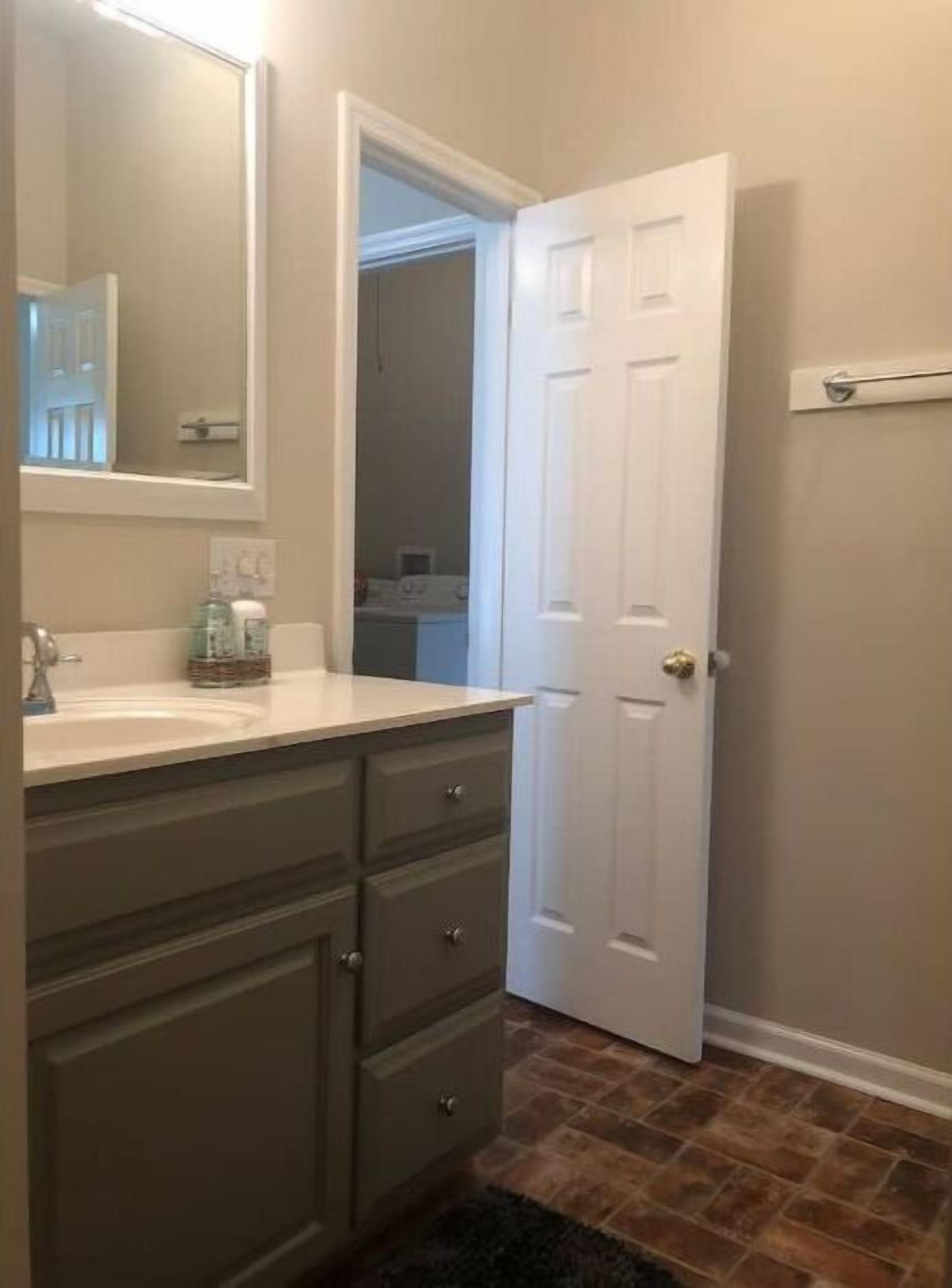 A bathroom with a white door, a sink with a mirror, and a dark-colored vanity.