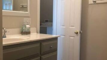 A bathroom with a white door, a sink with a mirror, and a dark-colored vanity.