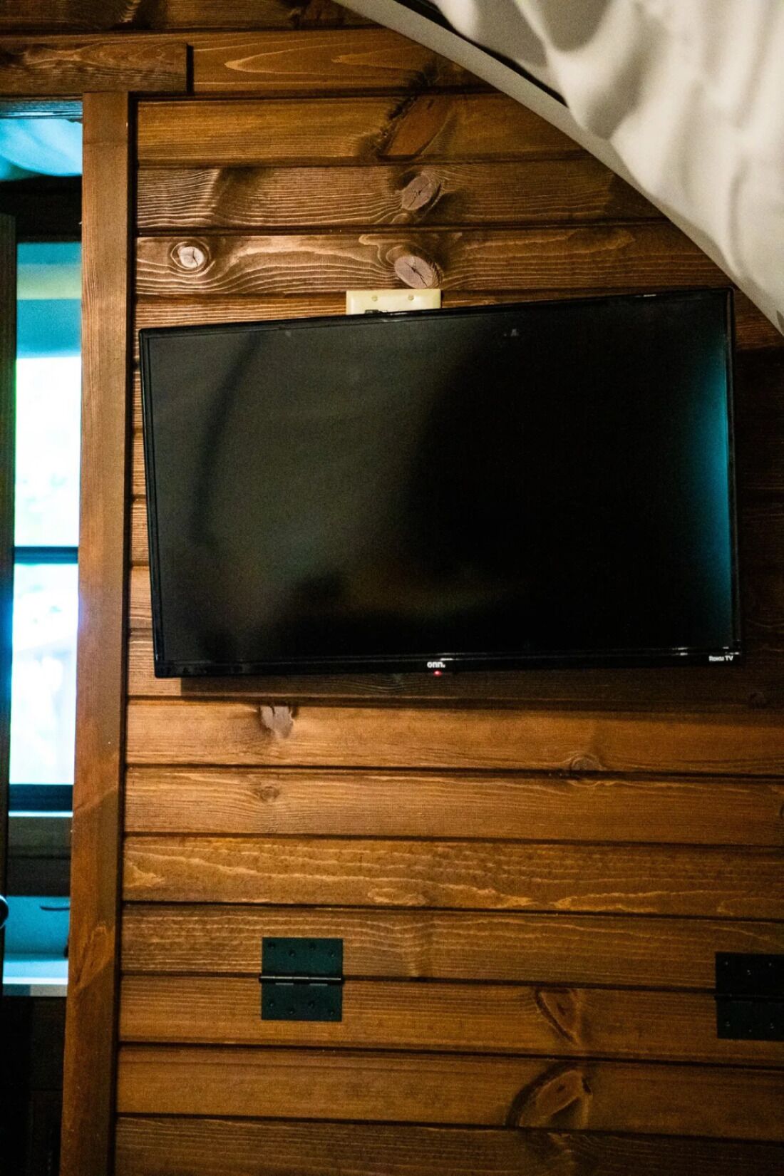 Ein Fernseher an einer Holzwand befestigt, darunter ein sichtbarer Stromanschluss.