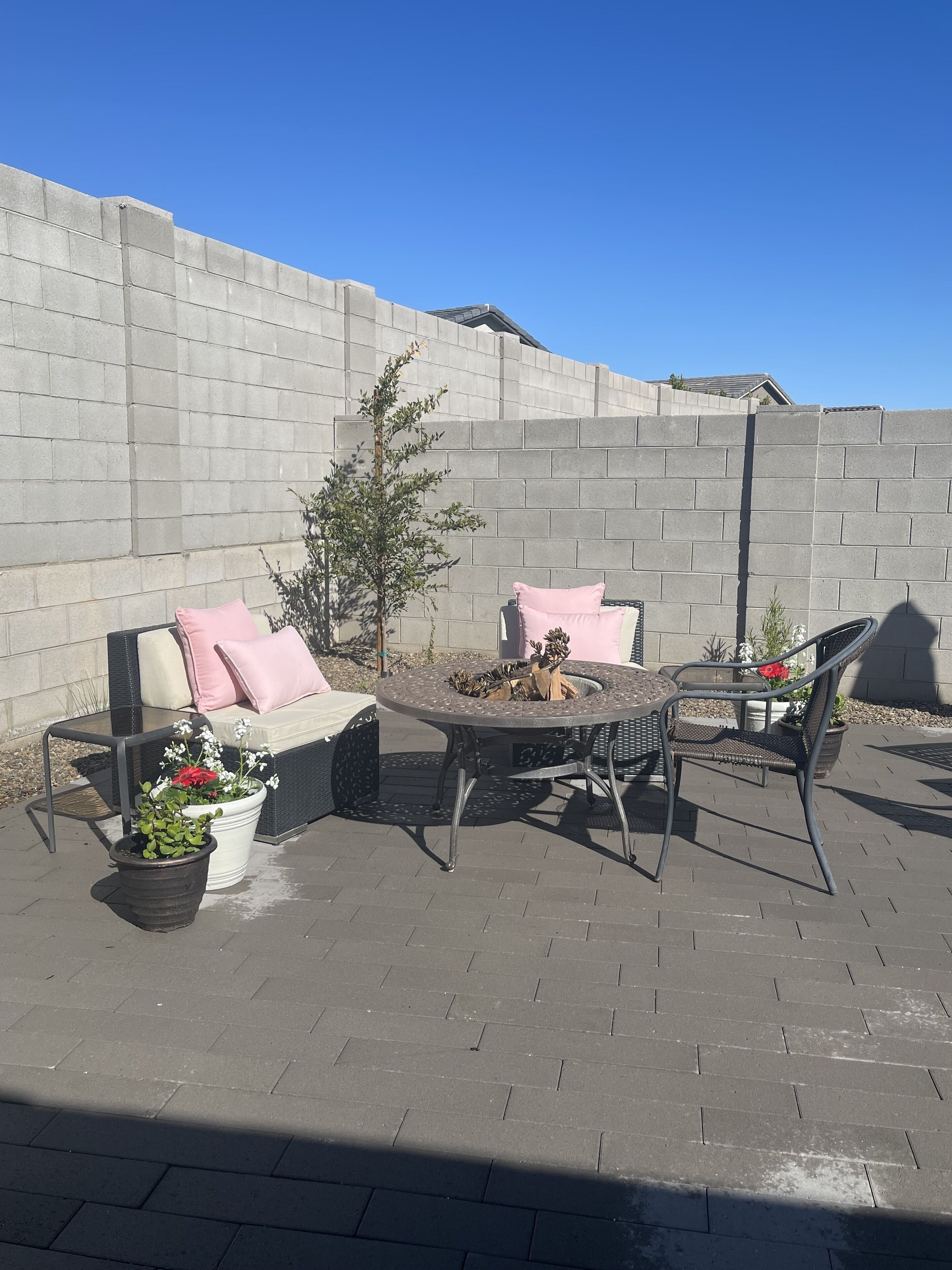 Une terrasse extérieure avec une table ronde, deux chaises, un canapé avec des coussins et des plantes en pot.