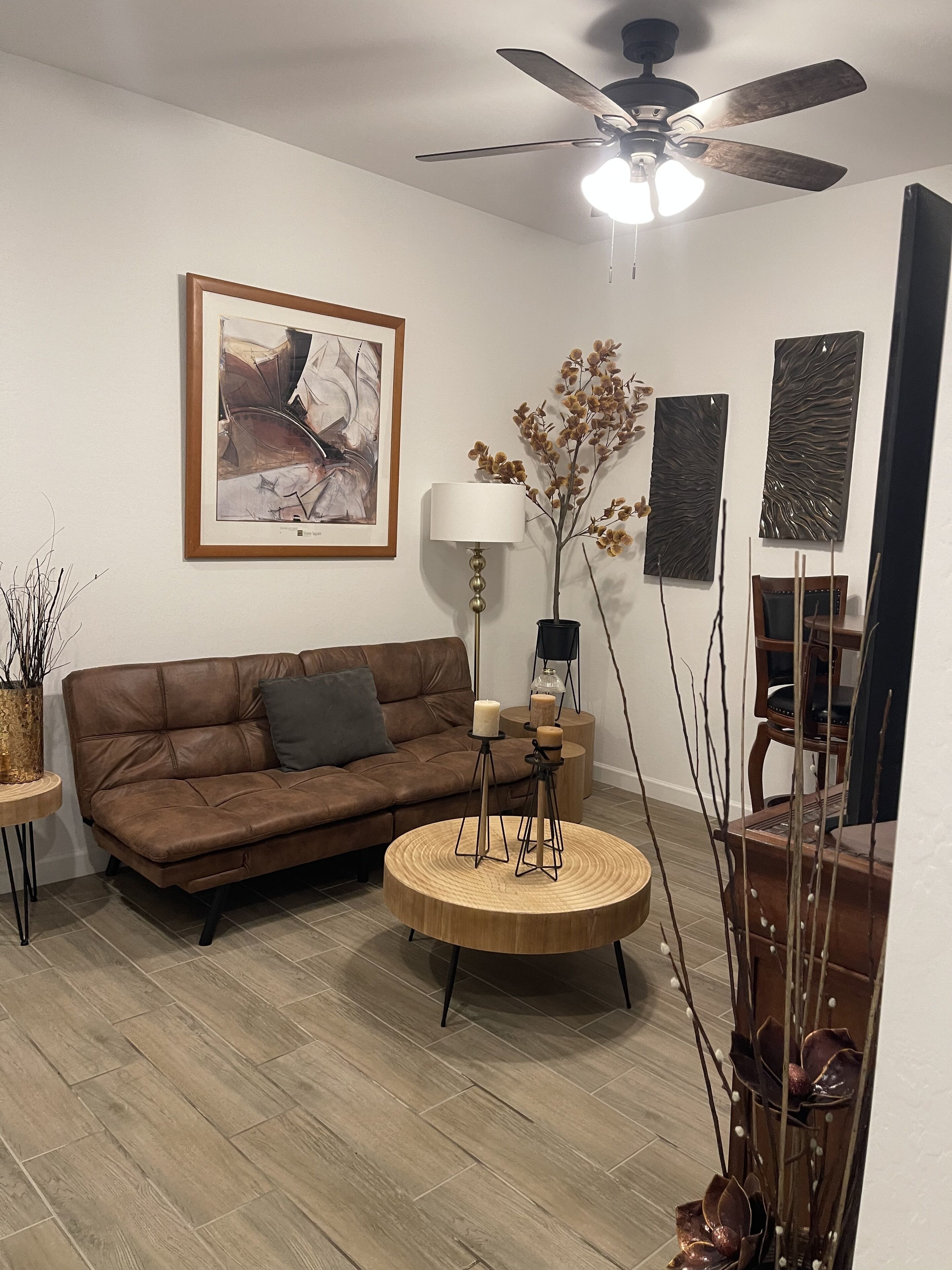 A modern living room with a brown leather sofa, a round wooden coffee table, a floor lamp, and a ceiling fan.