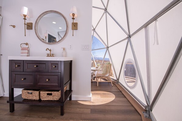 A modern bathroom with a dark wooden vanity, a round mirror, and wall-mounted lights.
