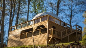 Una cabaña de madera con techo abovedado, ventanas amplias y una terraza de madera.