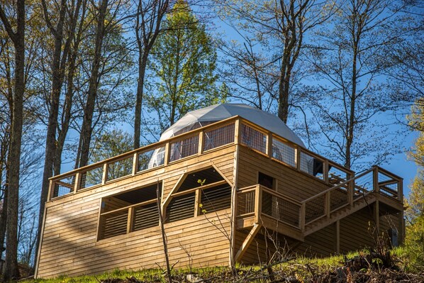 Una cabaña de madera con techo abovedado, ventanas amplias y una terraza de madera.