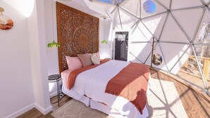 Un dormitorio con una estructura de techo geométrica, un cabecero de madera y una cama con colcha blanca y naranja.
